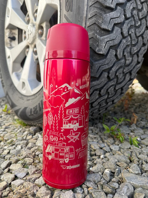 Red Zojirushi SJ-JS stainless steel vacuum bottle with camping and outdoor illustrations, standing on gravel beside a car tire. Capacity ranges from 800 ml (27.05 oz) to 1030 ml (34.85 oz).