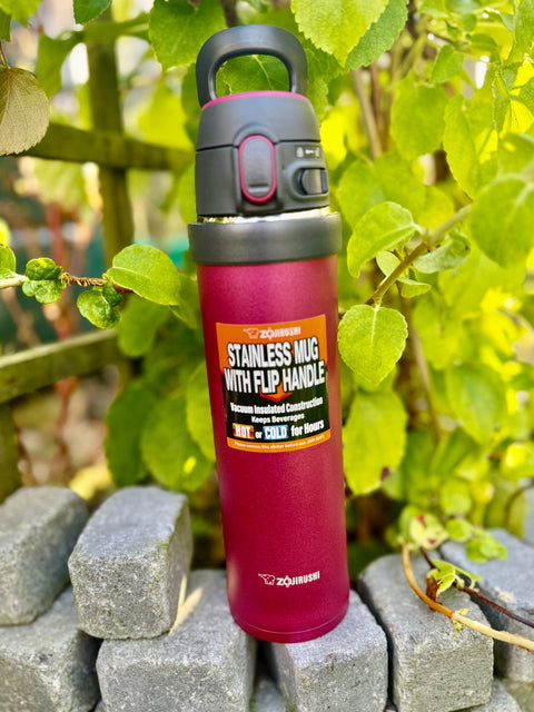 Zojirushi SM-QAF60 Carry Tumbler in Red, 600 ml stainless steel travel mug with flip handle, BPA-free insulated bottle for hot and cold drinks, photographed outdoors among green leaves