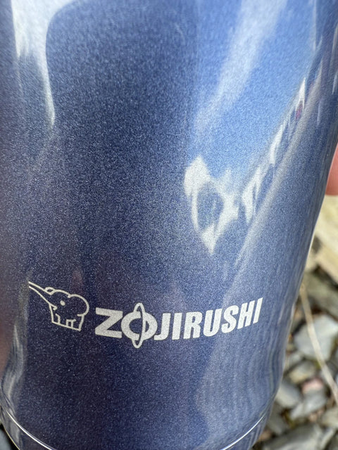 Zojirushi logo with elephant icon printed on a dark blue stainless steel thermal mug.