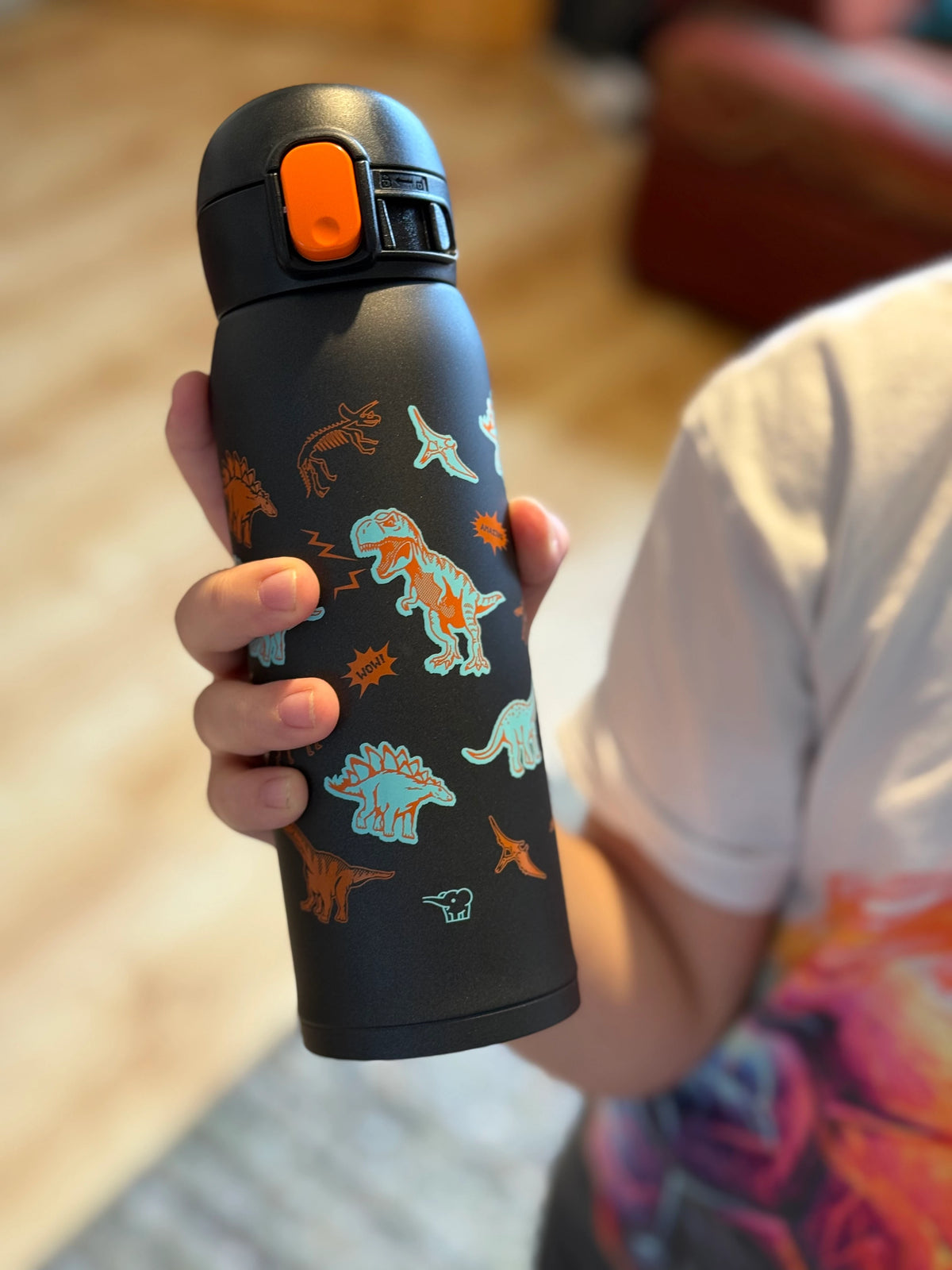 Eco-friendly Zojirushi SM-WM48BA 480 ml (16.20 oz) black insulated kids mug with colourful dinosaur design, stainless steel reusable bottle for school, hot and cold drinks, held by child indoors.