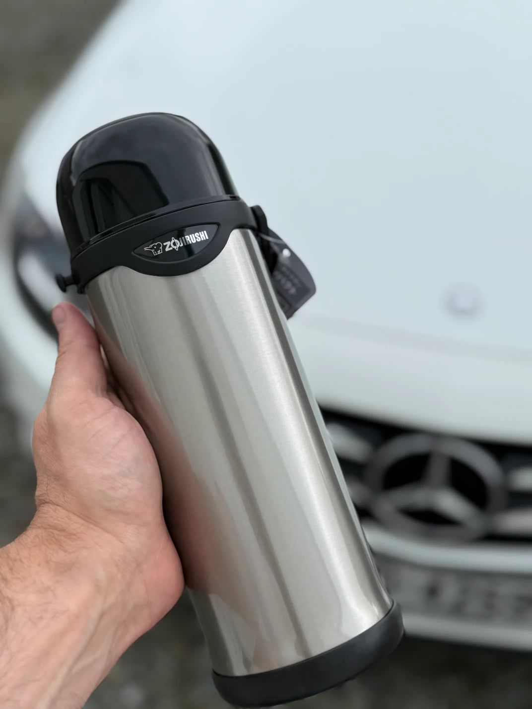 Zojirushi SJ-TG stainless steel bottle held in hand with a white Mercedes car in the background, 800 ml (27.05 oz) to 1000 ml (33.80 oz)