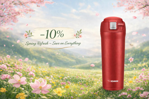 Red Zojirushi travel mug in a spring flower meadow with soft cherry blossoms and a subtle “-10% Spring Refresh” discount message on a pastel background