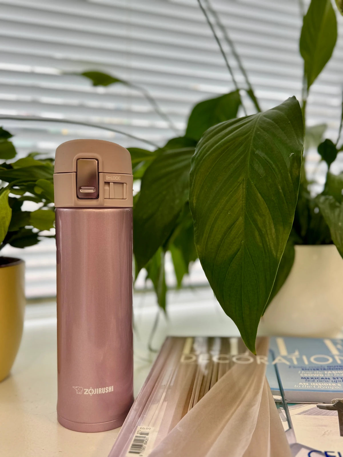 Zojirushi SM-KHE Pink travel mug on a desk with green plants and magazines, 360 ml (12.20 oz) to 480 ml (16.20 oz)