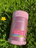 Zojirushi SW-EAE Pink 500 ml (16.9 oz) thermal food jar, stainless steel insulated lunch container photographed outdoors on green grass with a yellow flower.